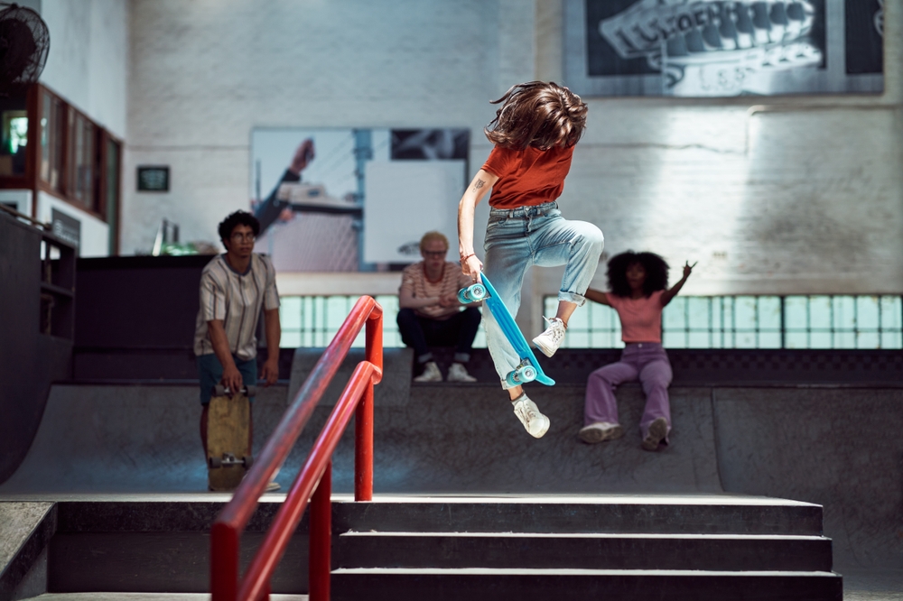 Skateboard Trick Over Stair Rail Indoors - Thomas Augusto Skateboarder performing a jump trick over a stair rail in an indoor skatepark with spectators. -Thomas Augusto