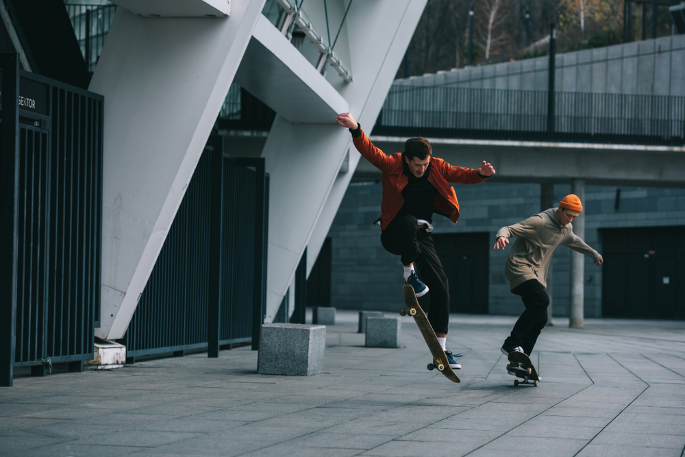 Skateboarders Performing Tricks in Modern Urban Plaza - Thomas Augusto Two skateboarders executing tricks in a sleek urban setting with modern architecture, showcasing street skateboarding style and movement. - Thomas Augusto